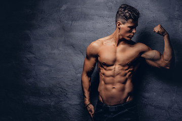 Fototapeta premium Strong shirtless young man model with nice muscular body showing his bicep at a studio.