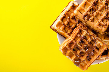 Belgian waffles on a plate of chopped chocolate on a yellow background. Sweets, dessert. Copy space