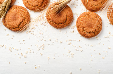 Oatmeal cookies with oat flakes and spikelets on a white wooden background. Copy space, top view.