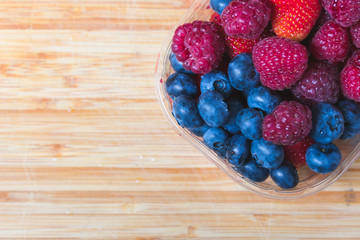 Close up and top view of mixed healthy fresh summer berries or food in glass bowls on wooden table or background. Healthy breakfast or summer diet plan to loose weight