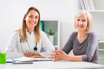 Portrait of female doctor and senior woman patient sitting in doctor's office.