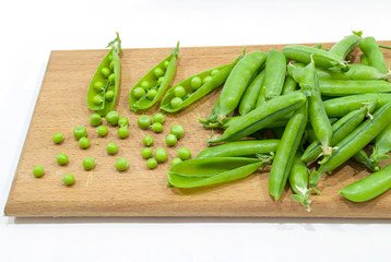 Fresh pods of sweet green peas in basket, on wooden board.