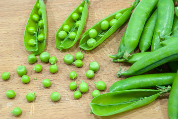 Fresh pods of sweet green peas in basket, on wooden board.