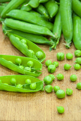 Fresh pods of sweet green peas in basket, on wooden board.