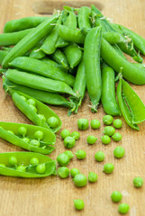 Fresh pods of sweet green peas in basket, on wooden board.