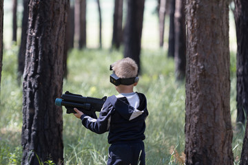 Young boy in camouflage with a gun, plays laser tag in the forest. Lasertag shooting game in open...