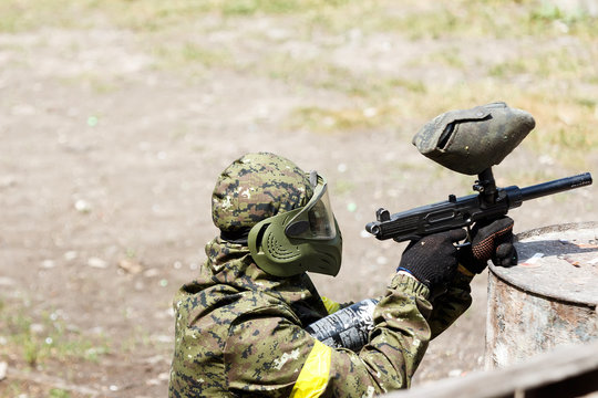Paintball player in protective uniform and mask aiming gun in the forrest cover. A young man is preparing to shoot. The concept of active recreation, team play. Selective focus