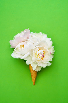 Waffle ice cream cone with white peony flowers on green background. Summer concept. Copy space, top view.