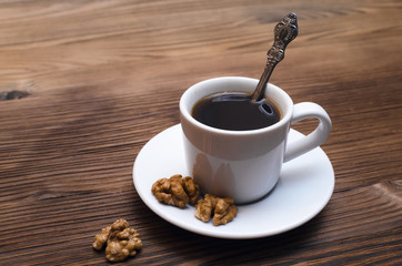 Cup of black coffee and with walnuts on the white plate on wooden kitchen table.