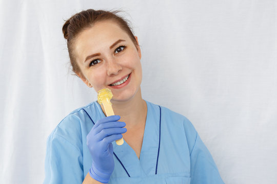 Smiling woman doctor beautician holds a spatula with sugar paste in her hand. Horizontal frame.