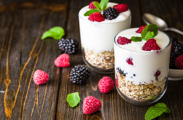 White yogurt with muesli and raspberries in glass bowl on rustic wooden background.