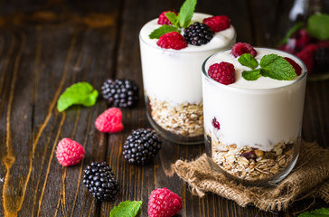 White yogurt with muesli and raspberries in glass bowl on rustic wooden background.