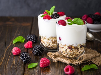White yogurt with muesli and raspberries in glass bowl on rustic wooden background.