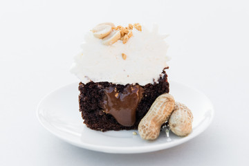 Cut of chocolate cupcake with cream and peanuts on a white plate. Close up