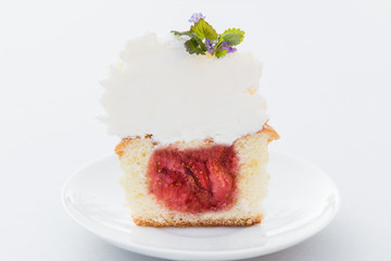 Cut strawberry cupcake with cream cheese and mint on a white plate. Close up