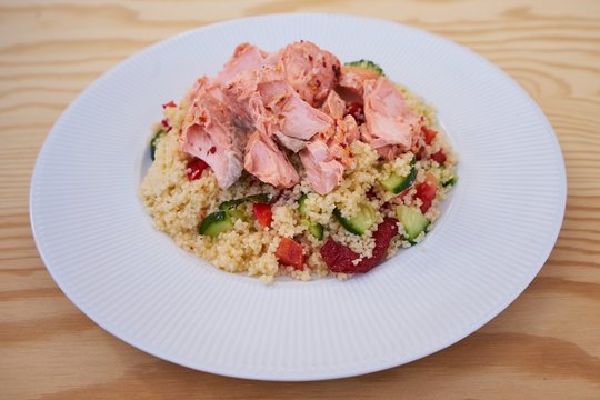 Detailed Picture of the fresh, tasty and healty couscous salad with poached salmon served on the simple white plate like light diner or lunch ideal for reduction diet.