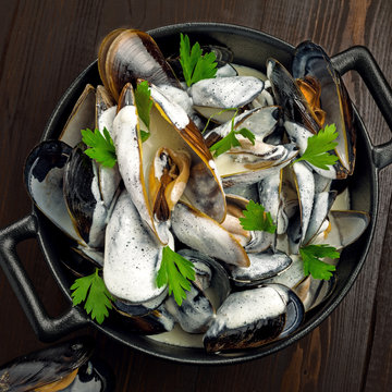 Moules marini&egrave;re with cream, garlic and parsley in a iron bowl. Delicious French food on a table. Top view.