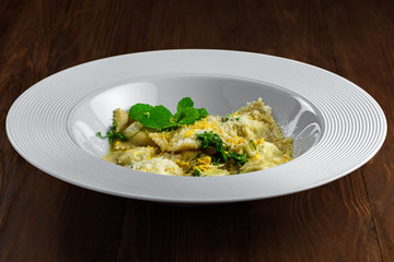 Delicious Italian ravioli with ricotta, mint and grated lemon rind served in a soup plate on a wooden table. Classic Italian cuisine food.