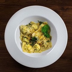 Ravioli filled with ricotta, mint and grated lemon rind on a rustic wooden table. Classic Italian cuisine pasta meal in a soup plate. Top view shot.