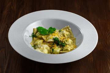 Gourmet Italian ravioli made of pasta dough, ricotta, mint and grated lemon served in a soup plate on a dark brown wooden table.