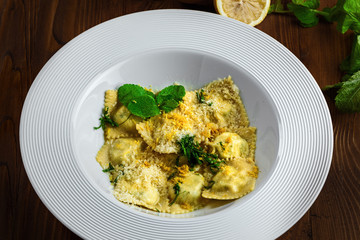 High class healthy Italian pasta meal on a wooden table. Excellent ravioli with ricotta, mint and grated lemon ring in a soup plate. Close-up shot.