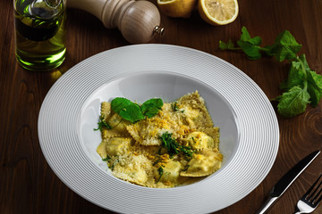 Tasty ravioli stuffed with ricotta, mint and grated lemon ring in a soup plate. First class Italian pasta food on a brown wooden table. Close-up shot.