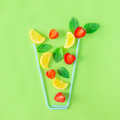 Creative layout strawberry lemonade ingredients - lemon, mint, berries falling in glass made with cocktail straws on green background. Summer drinks. Minimal food concept. Selective focus. Copy space.