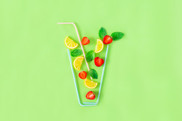 Fototapeta premium Creative layout strawberry lemonade ingredients - lemon, mint, berries falling in glass made with cocktail straws on green background. Summer drinks. Minimal food concept. Selective focus. Copy space.