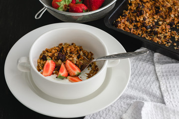 Breakfast of granola, yogurt and strawberries on a dark table.