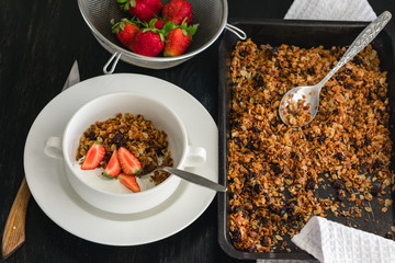 Breakfast of granola, yogurt and strawberries on a dark table.
