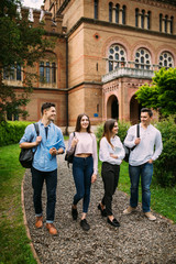 College students walking together outdoors. Group of young people in college campus University.