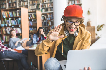 Portrait of outgoing male gesticulating hand while watching at laptop in library
