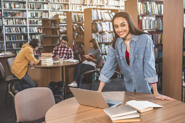 Portrait of beaming lady typing in digital device while standing at desk in athenaeum