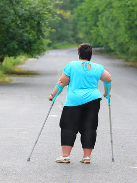 Overweight patient with crutches walking on footpath. Physiotherapy treatment and obesity problems.