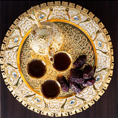 Traditional golden arabic coffee set with dallah, three cups of tea and dates. Dark background. Square image. Top view.