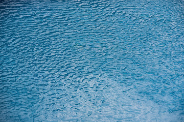 Water with small waves and raindrops on a pool with blue texture background