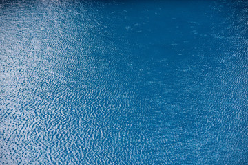 Water with small waves and raindrops on a pool with blue texture background
