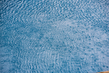 Water with small waves and raindrops on a pool with blue texture background