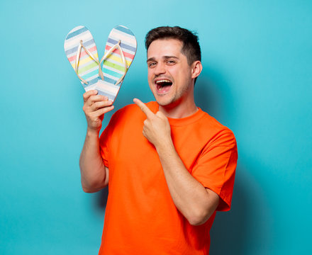 Young handsome man in orange t-shirt with sandals. Studio image on blue background