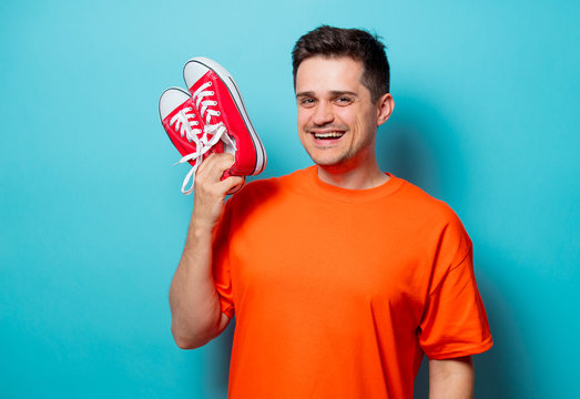 Young handsome man in orange t-shirt with red gumshoes. Studio image on blue background
