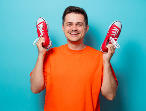 Young handsome man in orange t-shirt with red gumshoes. Studio image on blue background