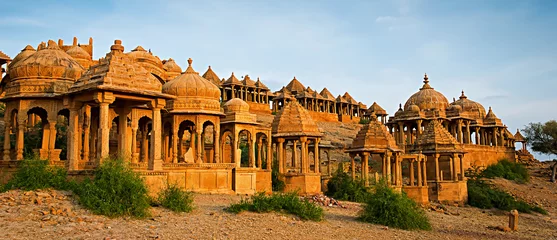 Fotobehang The royal cenotaphs of historic rulers, also known as Jaisalmer Chhatris, at Bada Bagh in Jaisalmer made of yellow sandstone at sunset © olenatur
