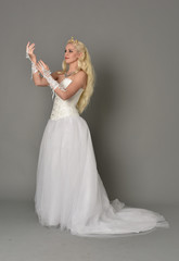Naklejka premium full length portrait of blonde girl wearing white fantasy gown. standing pose in side profile, grey studio background.