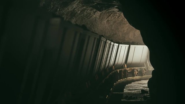 Full of coal mine wagons slowly moving through narrow underground tunnel.