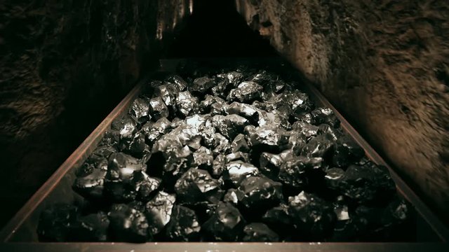 Top of a coal mine wagons slowly moving through narrow underground tunnel.