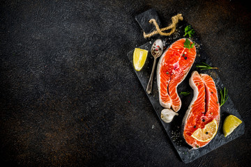 Raw salmon fish steaks with lemon, herbs, olive oil, ready for grill, slate cutting board, dark rusty background copy space