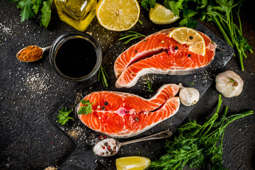 Raw salmon fish steaks with lemon, herbs, olive oil, ready for grill, slate cutting board, dark rusty background copy space