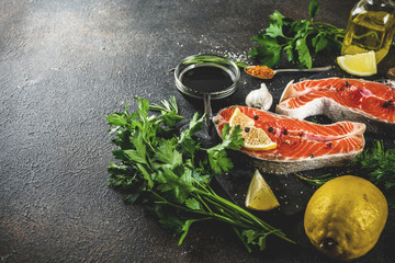 Raw salmon fish steaks with lemon, herbs, olive oil, ready for grill, slate cutting board, dark rusty background copy space