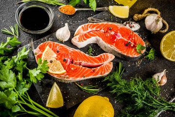 Raw salmon fish steaks with lemon, herbs, olive oil, ready for grill, slate cutting board, dark rusty background copy space