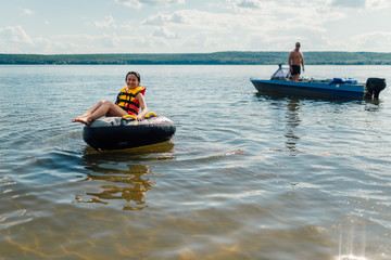   girl on the inflatable pillow is smiling, preparing to skate after the boat on the lake.